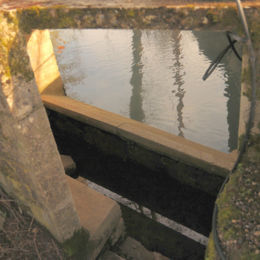 Lavoir aménagé contre un pont, sur la berge d'un cours d'eau, sur une retenue par vanne, permettant de réguler la hauteur de l'eau. Plusieurs marches font accéder à une petite niche, qui ne pouvait abriter que 2 lavandières au maximum. Deux pierres inclinées vers le cours d'eau permettent le lavage. . Le tout est couvert par une dalle en béton également.
06/2017 F Leng phot. 12 caue39 - GRUSSE (39190)