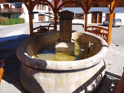 Fontaine borne de section carrée, surmontée d'un vase en pierre avec deux sorties d'eau. Située au centre d'un bassin ovale en pierres. L'édicule a été couvert par un artisan local
06/2017 F Leng phot. 02 caue39 - FONCINE-LE-HAUT (39460)