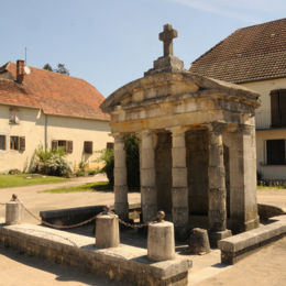 Sermange, mai 2012 F. Leng / CAUE39 : Fontaine monumentale en forme de façade de temple avec 4 piliers composites protégeant une très grande niche abritant un puisoir. Une croix en pierre repose sur l'ensemble. Cet aménagement ne comporte pas de bassin. - SERMANGE (39700)