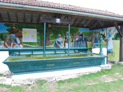 LA CHAUX-DU-DOMBIEF (39150), avril 2010 F. Leng / CAUE39 : Lavoir constitué par l'assemblage de 2 bassins rectangulaires en fonte. Le premier, sur la route, est un abreuvoir, le second, couvert, présente des barres de support pour une planche à laver périphérique. Il s'agit d'une réalisation de la fonderie de Varigney (Dampierre-les-Conflans (70)). L'ensemble a fait l'objet d'une restauration et d'une présentation avec des panneaux peints muraux représentant des lavandières en action. Le lavoir est implanté sous un bâtiment en bordure de route mais il ne s'agit pas de son emplacement d'origine.Le bâtiment se compose de 3 murs et de 2 piliers métalliques en façade, sur lesquels repose une charpente en bois, couverte de tuiles. L'aire de lavage est protégée de l'intrusion du bétail par 2 tourniquets latéraux en fonte. - LA CHAUX-DU-DOMBIEF (39150)