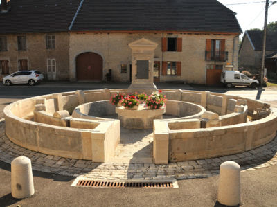 CERNANS (39110) sept 2011 F. Leng / CAUE39 : Fontaine-lavoir circulaire complexe, restaurée, dont la fontaine est formée d'une chèvre rectangulaire avec une applique de dauphin en fonte. Le circuit de l'au est remarquable et original. La fontaine alimente un petit puisoir accessible depuis l'extérieur, d'où l'eau se répartit dans 2 bassins circulaires étroits, concentriques, répartis autour d'un emplacement central, également circulaire. Le muret du bassin interne présente des pierres inclinées vers l'eau, caractéristique des lavoirs. Les lavandières se tenaient donc à l'intérieur pour laver, alors que le bassin externe devait servir d'abreuvoir. La fontaine-lavoir date de 1840, elle est due à l'architecte Narcisse Perrard - CERNANS (39110)
